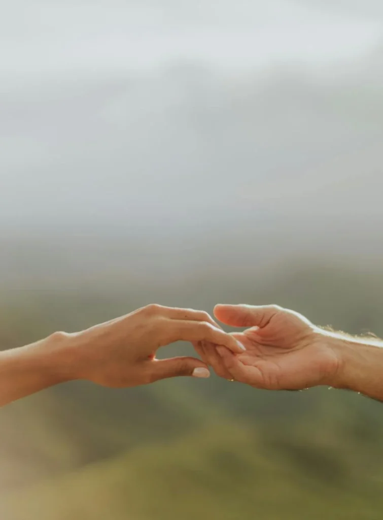 Two hands gently reaching towards each other against a blurred natural background.